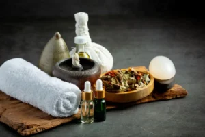 A collection of wellness items including herbal tea, essential oils, a towel, and a massage stone on a wooden surface.