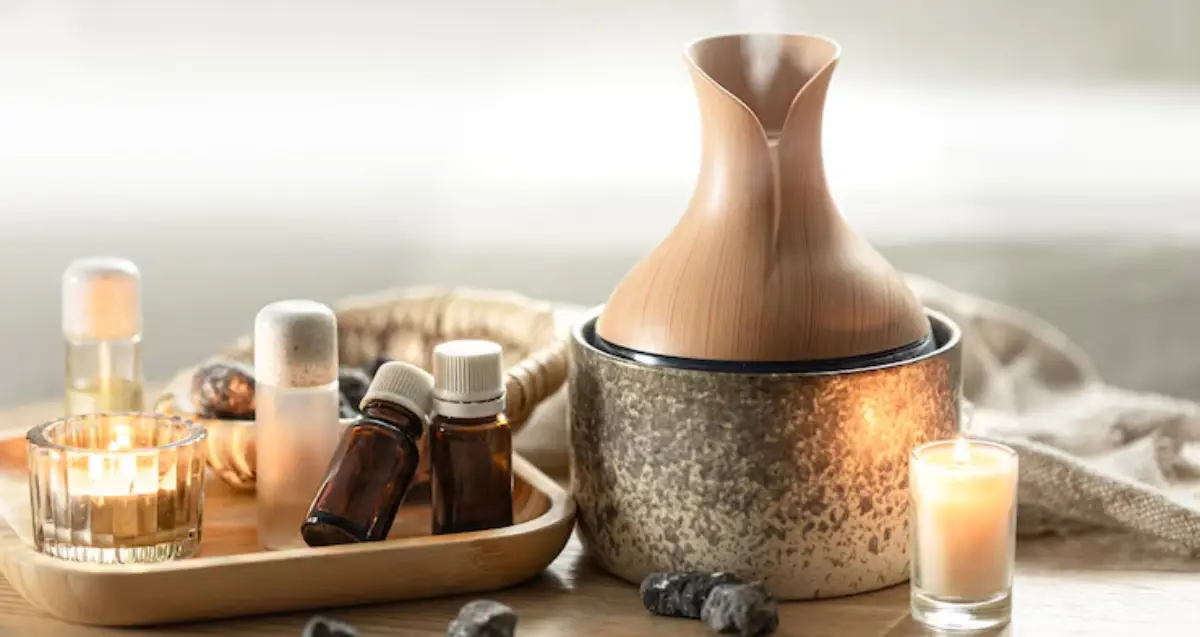 A bamboo essential oil diffuser surrounded by candles and various essential oil bottles on a wooden surface, creating a serene atmosphere.