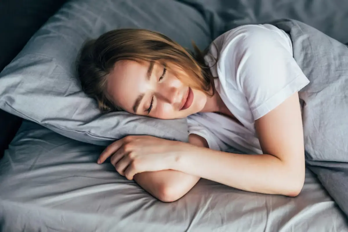A person lying on their side on a bed, resting peacefully on a gray pillow, with soft bedding surrounding them.