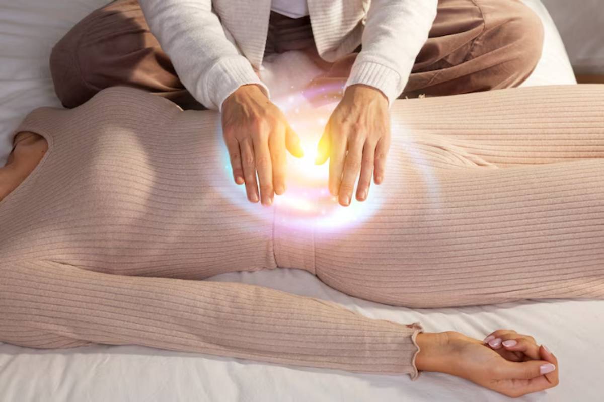 A practitioner performs energy healing by placing hands above a woman's abdomen, with a glowing aura effect between them.