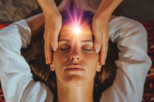 A person receives a healing or massage treatment, with hands gently placed on their head, radiating soothing light.