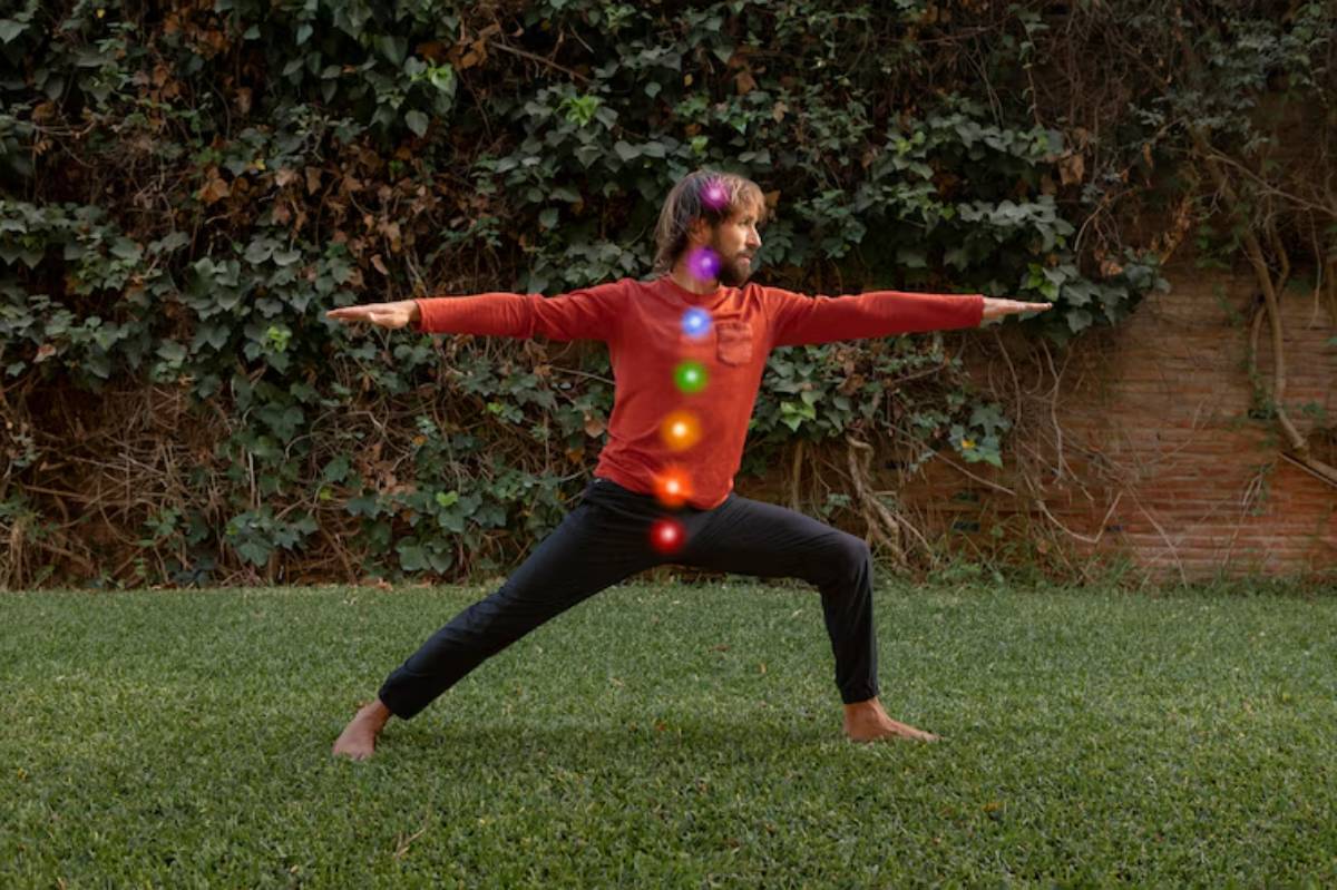 A person in a red shirt performs a yoga pose on grass, with brightness and energy symbols representing chakras aligned along their body.