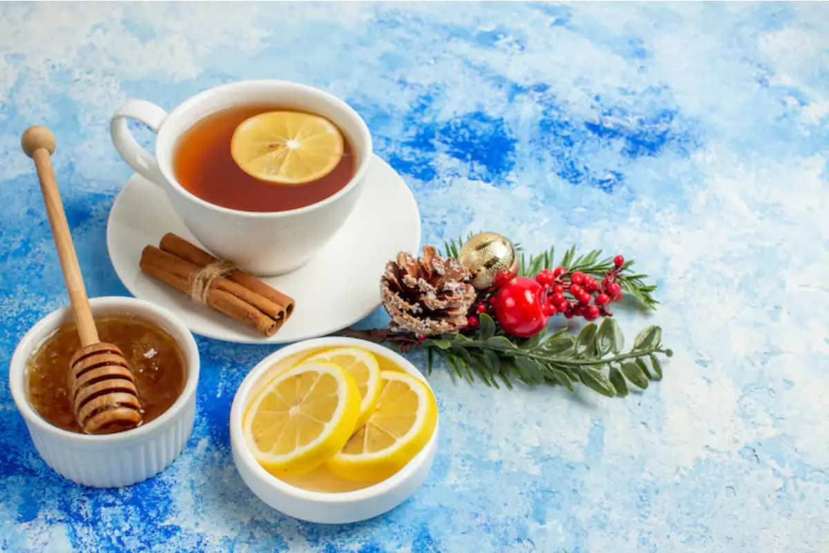 A cozy scene featuring a steaming cup of tea with lemon, honey, cinnamon sticks, fresh lemon slices, and festive decorations on a blue background.
