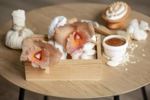 A wooden box with fluffy white towels and vibrant pink mushrooms, surrounded by spa essentials on a small round table.
