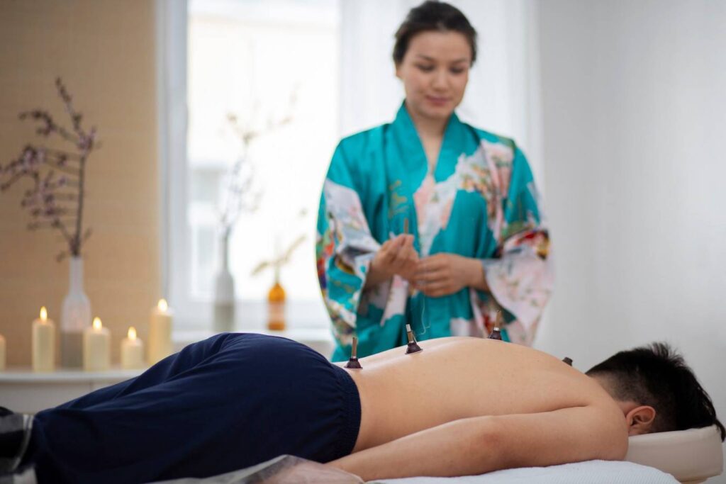 A person receiving cupping therapy in a serene room with candles, while a practitioner in a kimono prepares to assist.