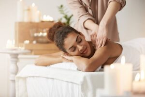 A relaxing spa scene with candles, a massage therapist gently working on a client's shoulders while they lie on a treatment table.