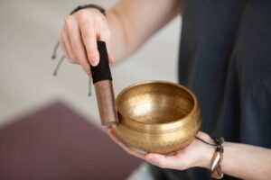 A person holds a brass singing bowl with a wooden mallet, preparing to create sound, in a calm, minimalist setting.