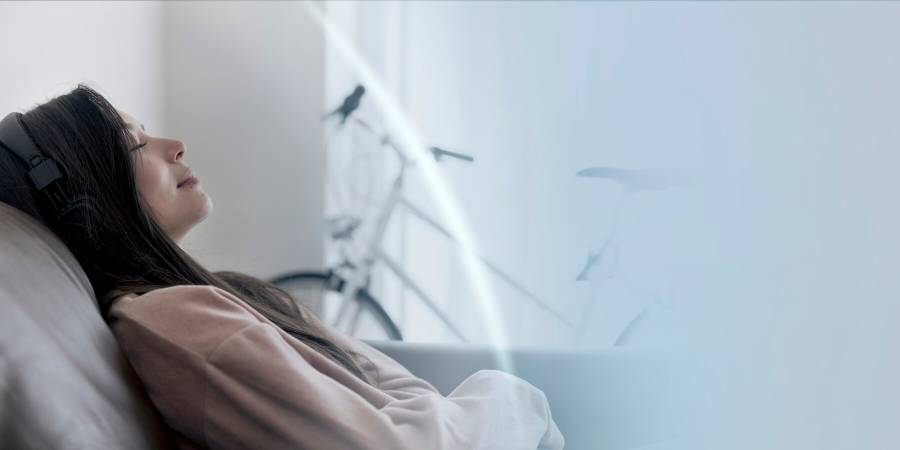 A person in a cozy living room wears headphones, relaxing on a couch, with a bicycle visible in the background.