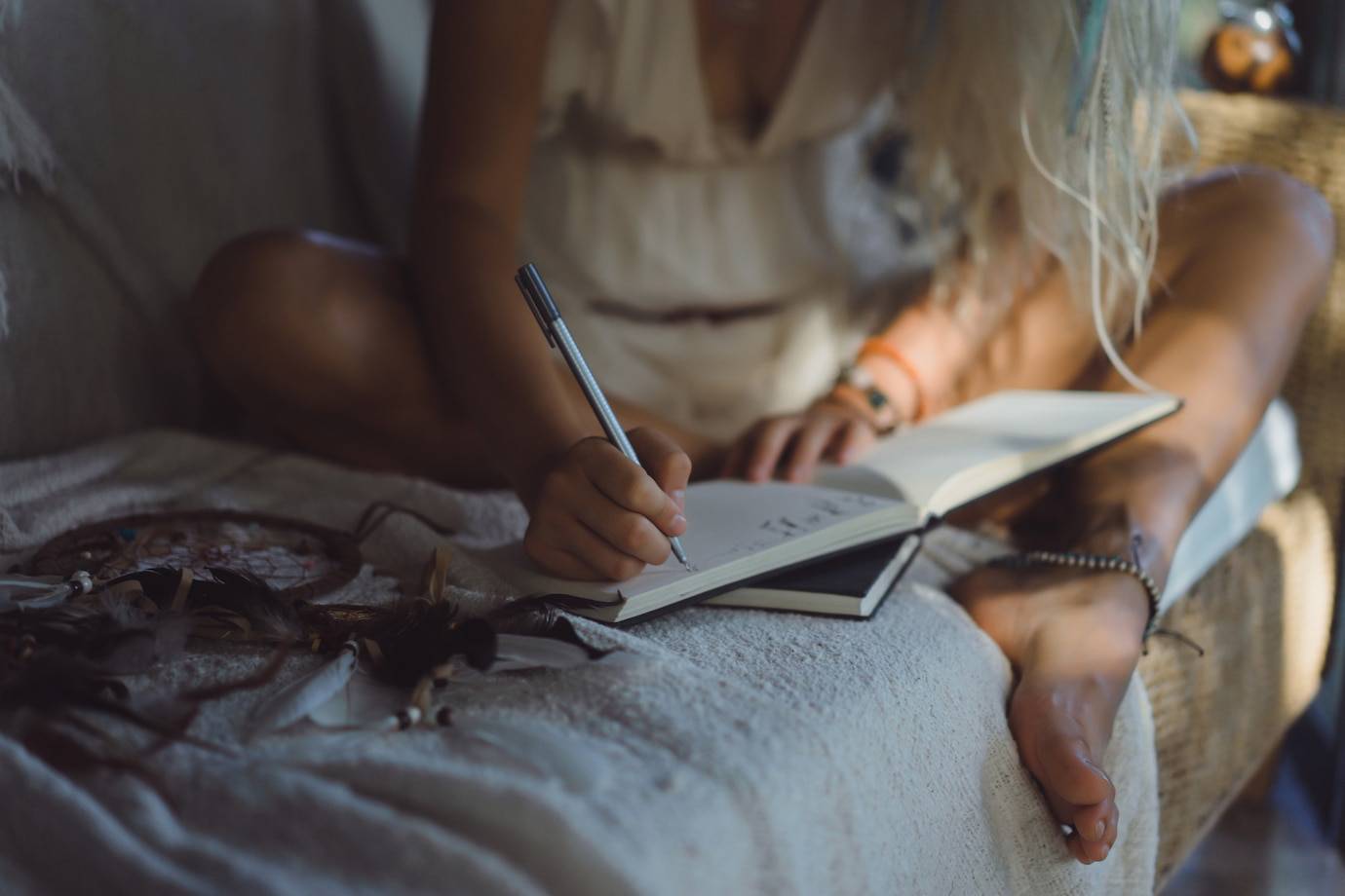 A person sitting on a couch, writing in a notebook with a pen, surrounded by natural decor and soft textiles.