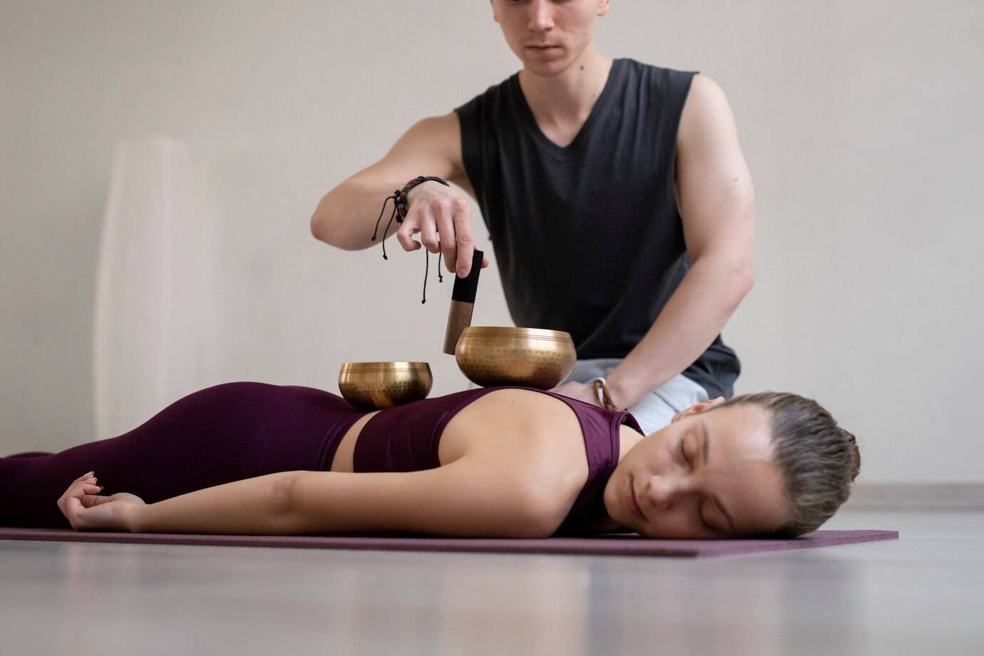 A person applies sound healing techniques using Tibetan singing bowls on a mat in a serene, minimalist setting.
