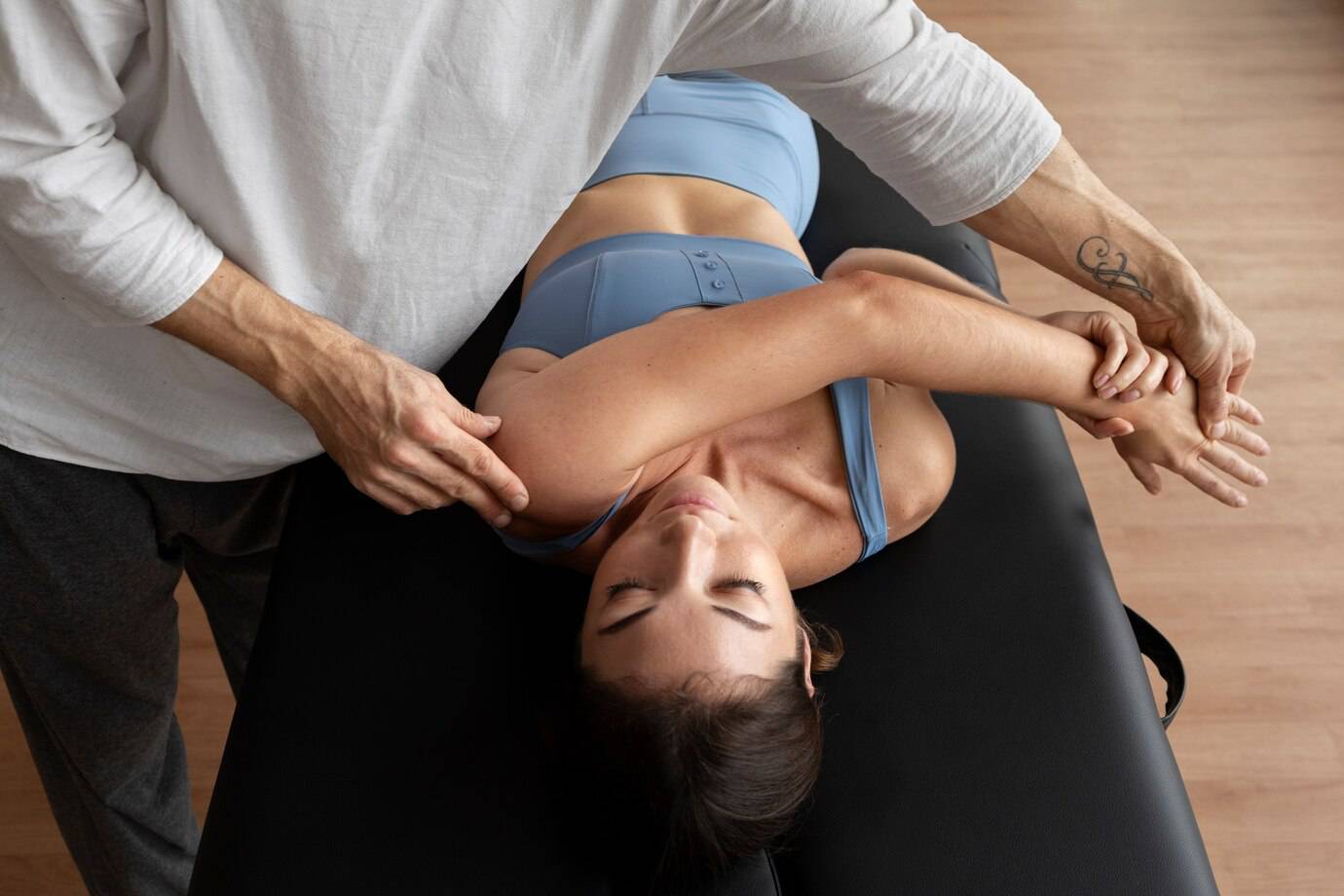 A person receives a therapeutic shoulder stretch from a practitioner on a massage table in a calm, wellness-focused environment.