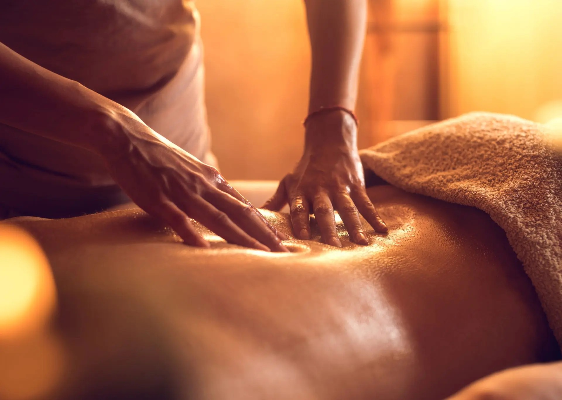 A massage therapist's hands apply oil on a client's back in a softly lit spa environment, promoting relaxation and wellness.