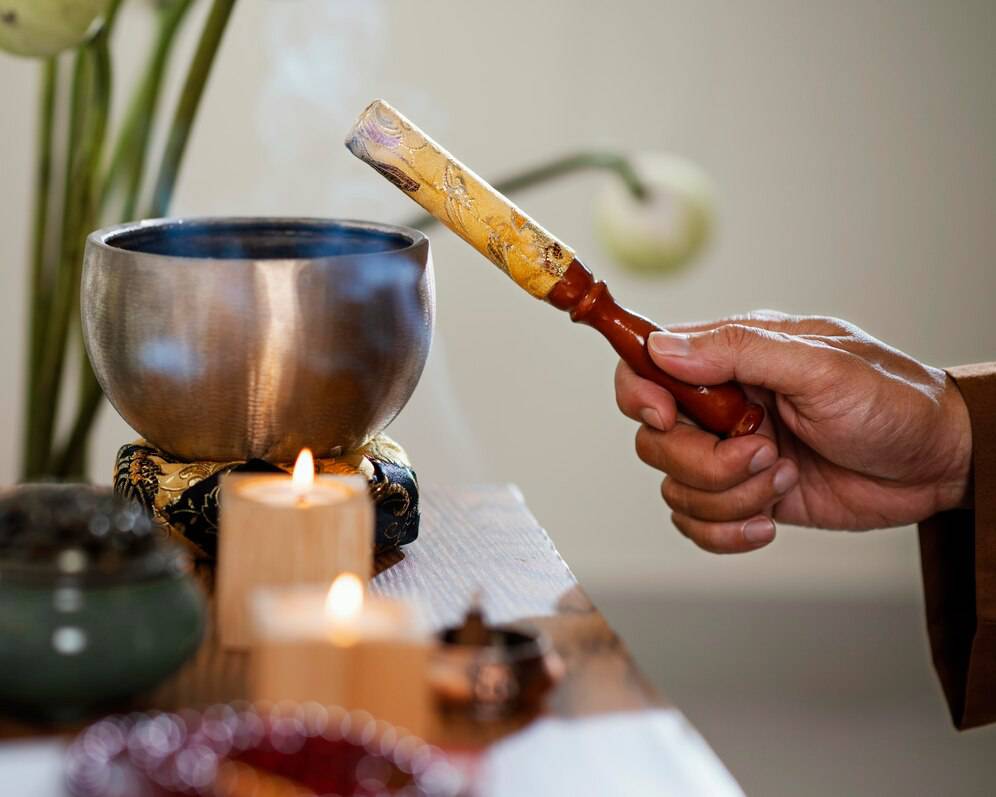 A hand holds a golden stick, guiding smoke from a silver bowl, amidst candles and a serene, tranquil setting.