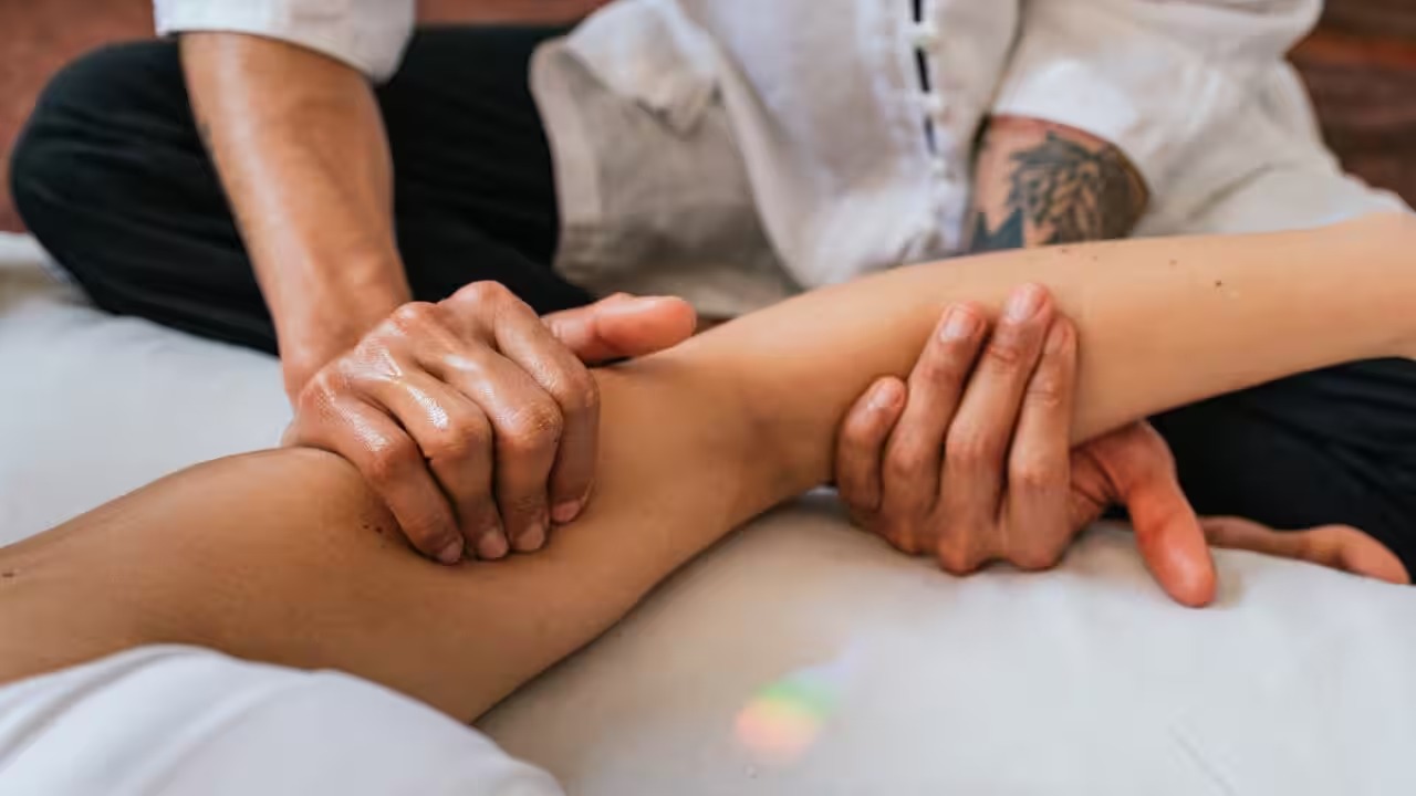 A close-up of a person receiving a massage on their forearm, with the therapist's hands applying gentle pressure.