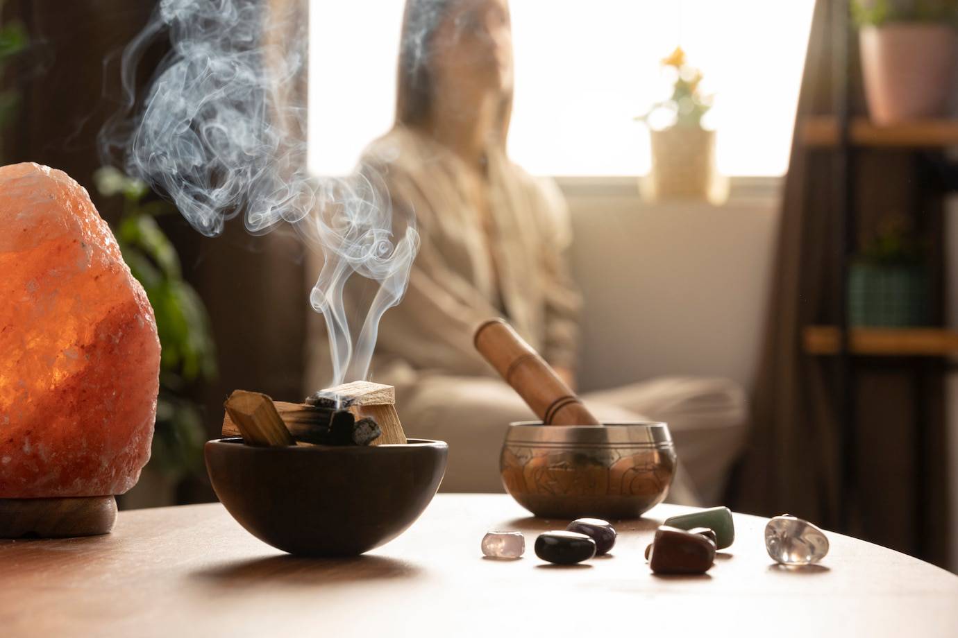 A calming interior scene featuring a bowl of incense smoke, a Himalayan salt lamp, and a person meditating in soft, natural light.